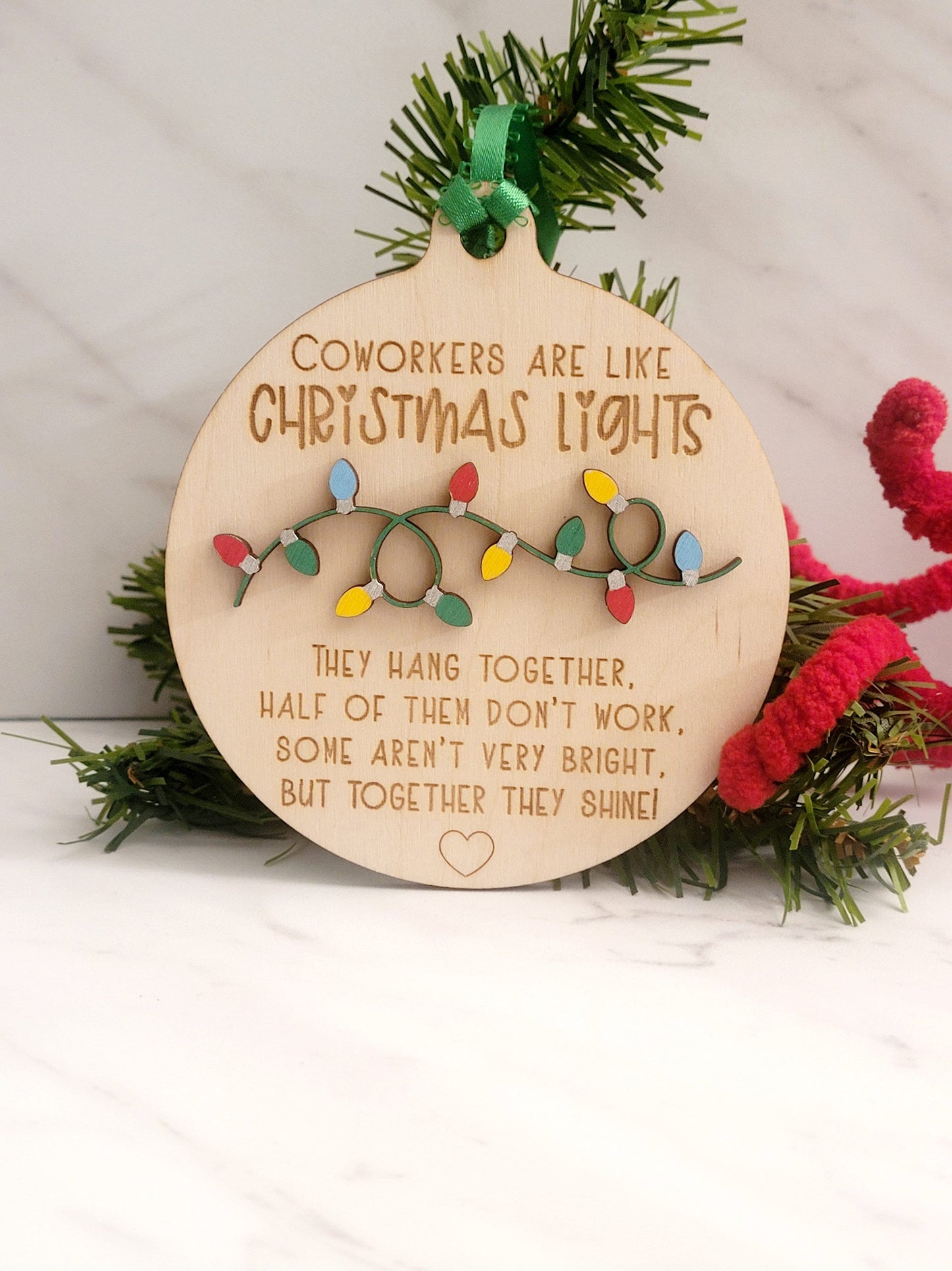 Round light wood ornament, with 3D strand of painted Christmas bulbs with engraved words "Coworkers are like Christmas lights they hang together half of them don't work, some aren't that bright but together they shine" with a heart on the bottom.