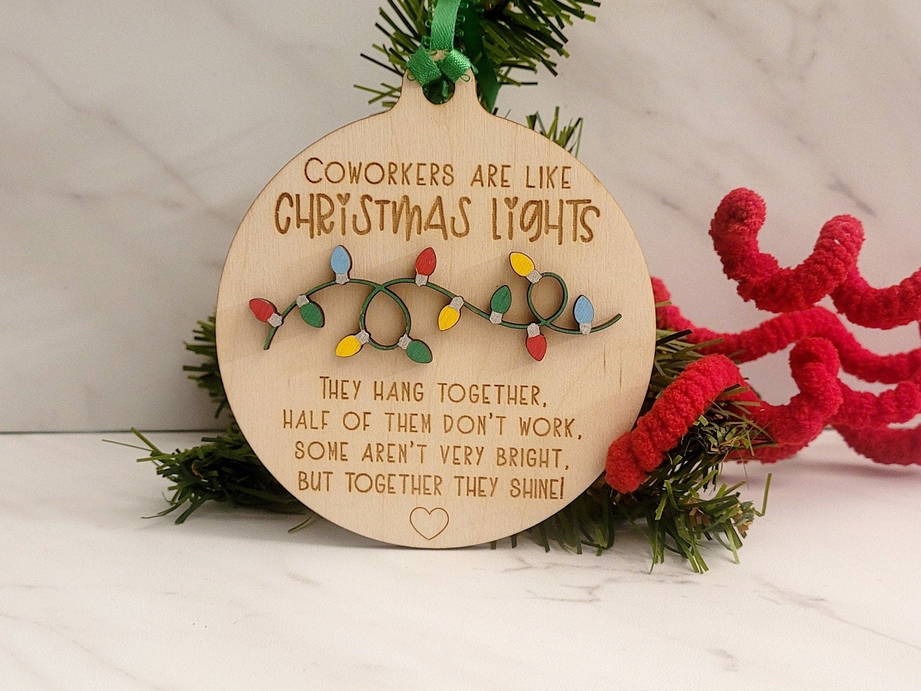 Light round ornament standing up against a piece of pine tree and a red fuzzy pick with a green satin ribbon.